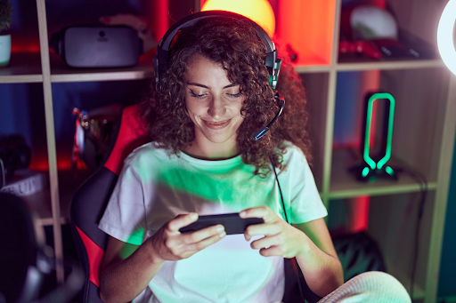 A smiling woman wearing a headset and playing a mobile game in a colorful neon-lit space