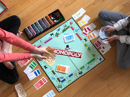 Two people sitting on the floor and playing Monopoly, holding cards and money in their hands.